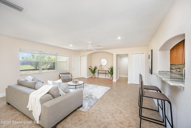 living area with arched walkways, a ceiling fan, light tile patterned floors, recessed lighting, and baseboards