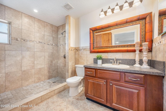 bathroom featuring toilet, a tile shower, tile walls, vanity, and a textured ceiling