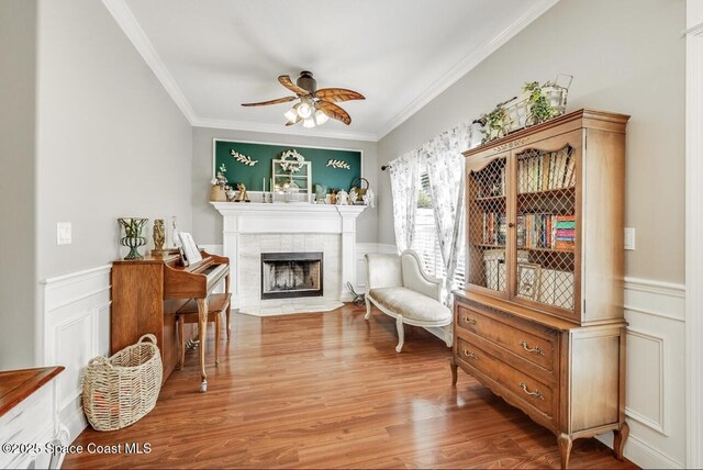 1409 Corbett Ln, Melbourne, FL 32904 - sitting room featuring ornamental molding, ceiling fan, wood finished floors, a tiled fireplace, and a wainscoted wall