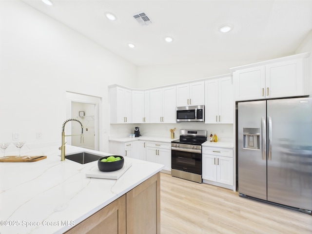 8126 97th Ave, Vero Beach, FL 32967 - kitchen featuring stainless steel appliances, a sink, light stone countertops, light wood-type flooring, and white cabinetry