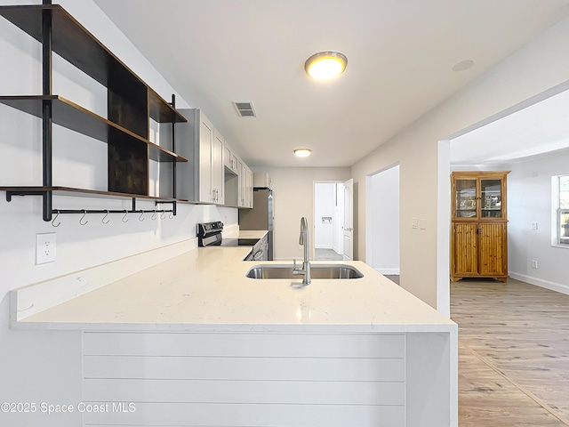 kitchen with a sink, stainless steel appliances, light wood-style floors, light stone counters, and a peninsula