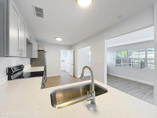 kitchen with electric stove, a sink, light wood-style flooring, and light stone counters