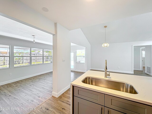kitchen featuring a sink, open floor plan, light wood-type flooring, gray cabinetry, and light countertops