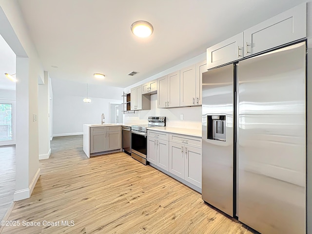 kitchen with stainless steel appliances, gray cabinetry, a sink, light wood finished floors, and baseboards