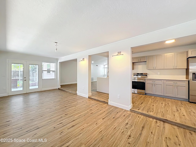 unfurnished living room featuring light wood-type flooring, baseboards, french doors, and a textured ceiling