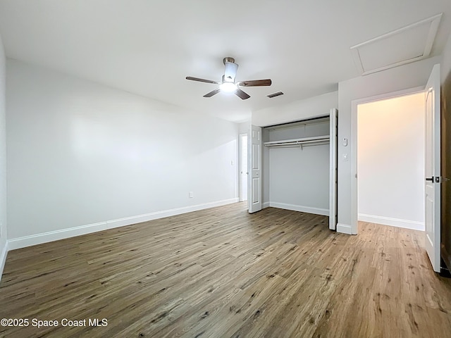 unfurnished bedroom with wood finished floors, attic access, baseboards, and a closet