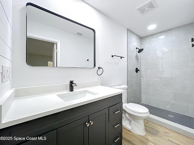 bathroom with toilet, wood finished floors, vanity, a tile shower, and recessed lighting