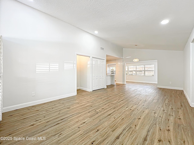 unfurnished living room featuring wood finished floors, a textured ceiling, baseboards, recessed lighting, and high vaulted ceiling