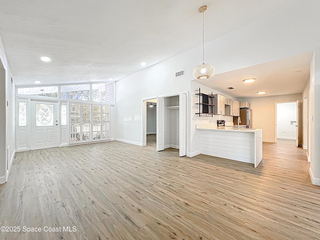 unfurnished living room with light wood-style floors, baseboards, a sink, and recessed lighting