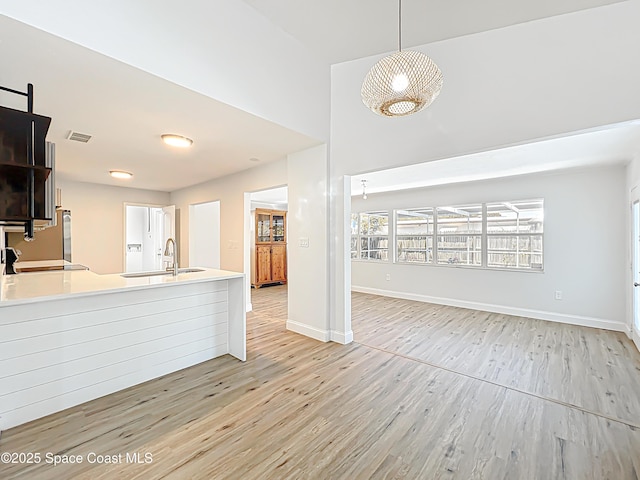 kitchen featuring a sink, light wood-style floors, a high ceiling, baseboards, and light countertops