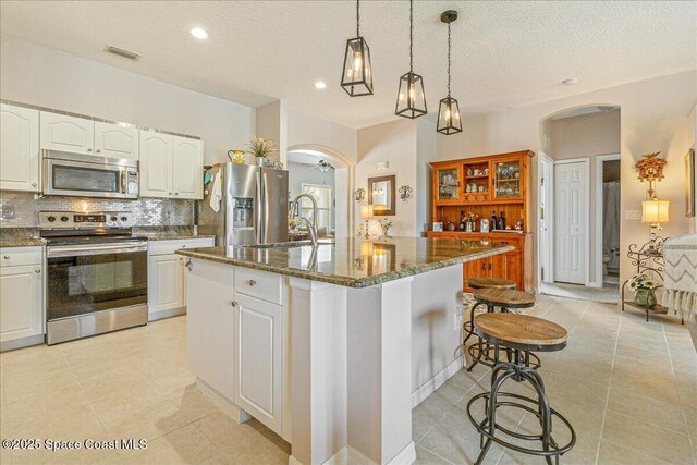 5290 Cinnamon Fern Blvd, Cocoa, FL 32927 - kitchen featuring appliances with stainless steel finishes, arched walkways, tasteful backsplash, dark stone countertops, and a center island with sink