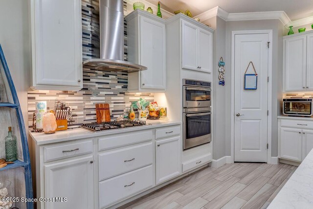 5250 Riveredge Dr, Titusville, FL 32780 - kitchen with wall chimney range hood, stainless steel appliances, white cabinetry, light countertops, and ornamental molding