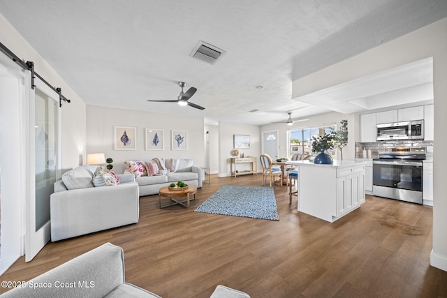 living area with a ceiling fan, a barn door, and wood finished floors