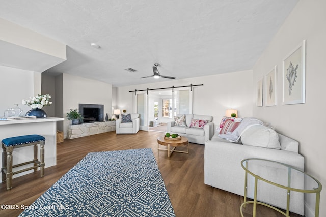 living area with wood finished floors, a barn door, a fireplace, and ceiling fan