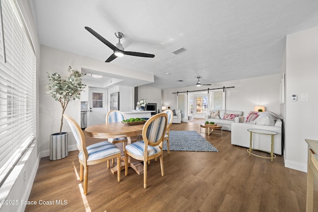 dining area with a barn door, ceiling fan, baseboards, and wood finished floors
