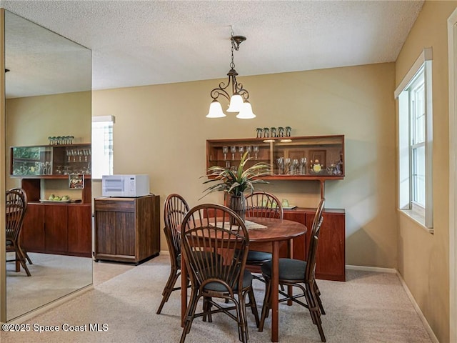 carpeted dining room with a textured ceiling, a chandelier, and baseboards