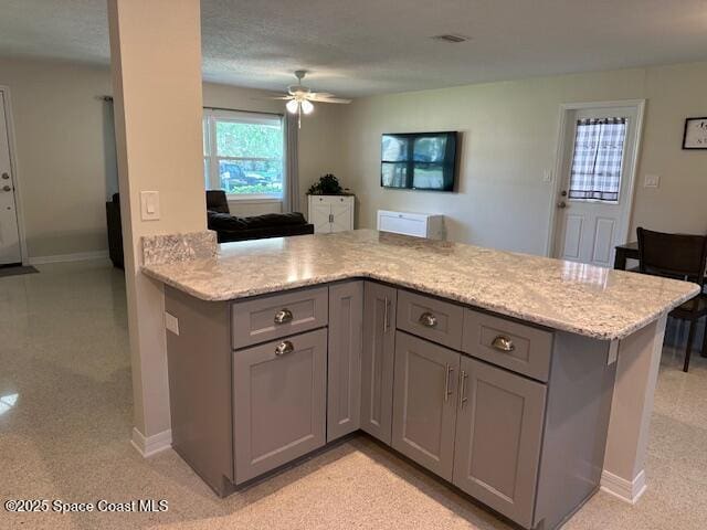 kitchen featuring gray cabinets, ceiling fan, baseboards, and light stone countertops