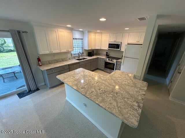 kitchen with appliances with stainless steel finishes, a sink, gray cabinets, recessed lighting, and light stone counters