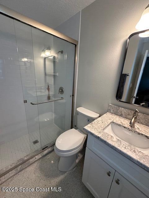 bathroom with a stall shower, toilet, vanity, and a textured ceiling