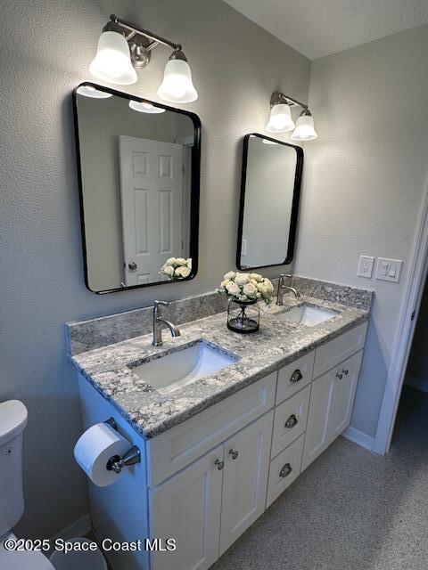 bathroom featuring toilet, double vanity, and baseboards