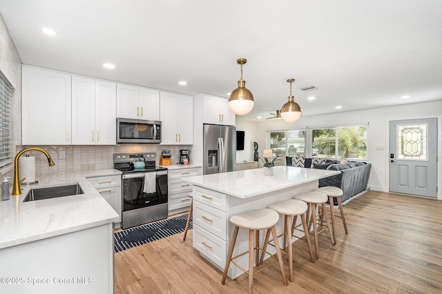 8103 Magnolia Ave, Cape Canaveral, FL 32920 - kitchen with appliances with stainless steel finishes, a sink, light wood-style flooring, a breakfast bar area, and white cabinetry