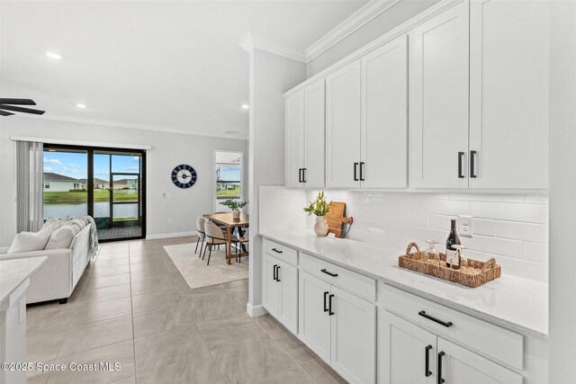 8854 Alister Dr, Melbourne, FL 32940 - kitchen featuring crown molding, open floor plan, decorative backsplash, baseboards, and white cabinets
