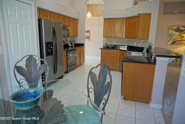 kitchen featuring appliances with stainless steel finishes, a sink, dark countertops, a peninsula, and brown cabinets