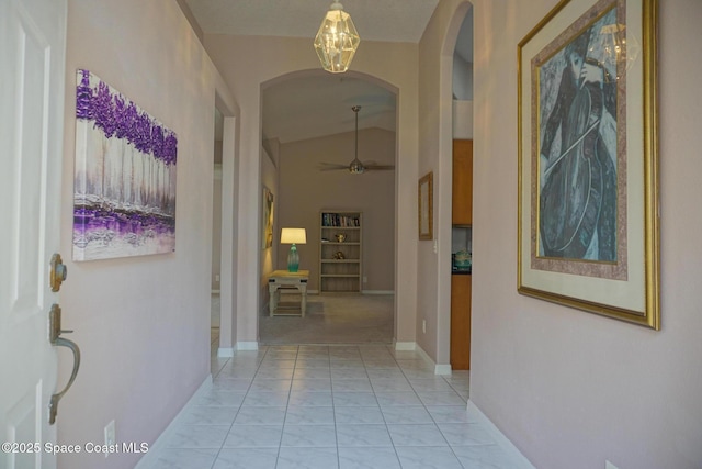 hallway with arched walkways, lofted ceiling, and baseboards
