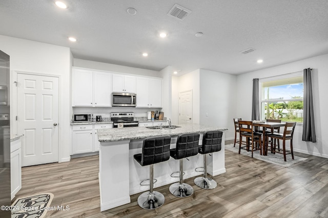 1717 Dalroy St NW, Palm Bay, FL 32907 - kitchen with stainless steel appliances, light wood finished floors, a sink, a kitchen island with sink, and white cabinetry
