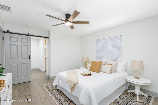 1020 Sycamore Dr, Rockledge, FL 32955 - bedroom with a barn door, light wood-type flooring, baseboards, and a ceiling fan