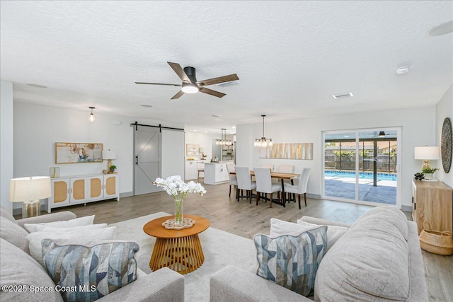 1020 Sycamore Dr, Rockledge, FL 32955 - living area featuring a barn door, a ceiling fan, light wood finished floors, a textured ceiling, and a chandelier