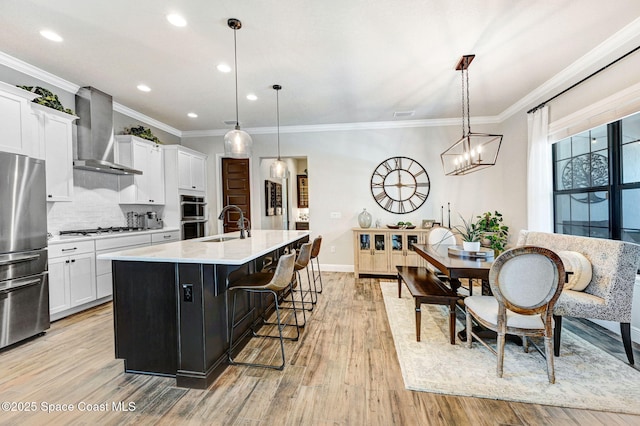 2291 Trava Ln, Melbourne, FL 32940 - kitchen featuring wall chimney range hood, stainless steel appliances, a sink, a kitchen island with sink, and white cabinetry