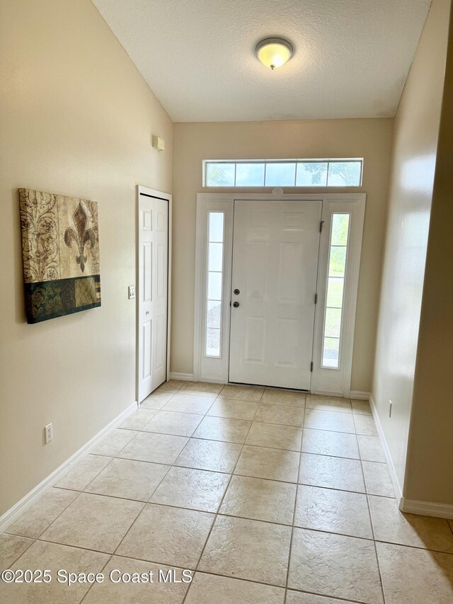 2601 Diane Ave SE, Palm Bay, FL 32909 - entryway featuring a textured ceiling, light tile patterned flooring, baseboards, and lofted ceiling