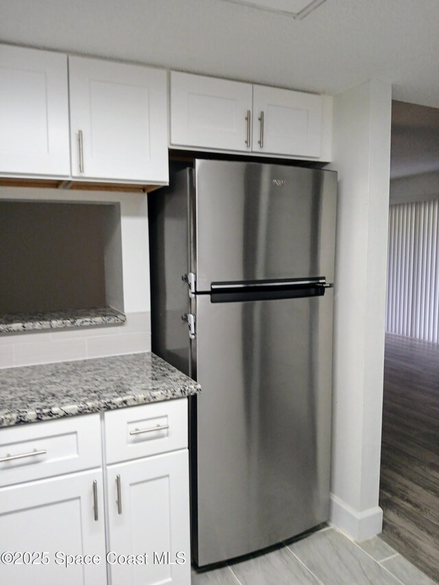 1641 Sunny Brook Ln NE Unit C110, Palm Bay, FL 32905 - kitchen featuring freestanding refrigerator, light stone counters, white cabinetry, and baseboards