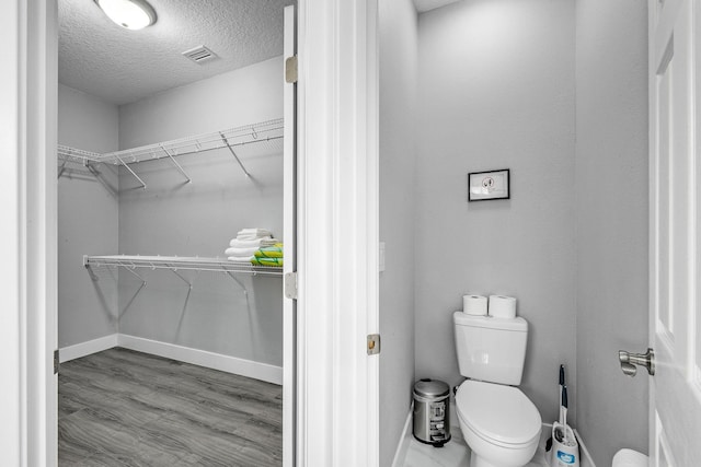 382 Eldron Blvd NE, Palm Bay, FL 32907 - bathroom with toilet, a textured ceiling, a walk in closet, baseboards, and wood finished floors