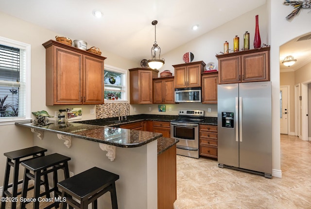 210 Sutton St, Rockledge, FL 32955 - kitchen featuring appliances with stainless steel finishes, a peninsula, brown cabinetry, dark stone counters, and vaulted ceiling