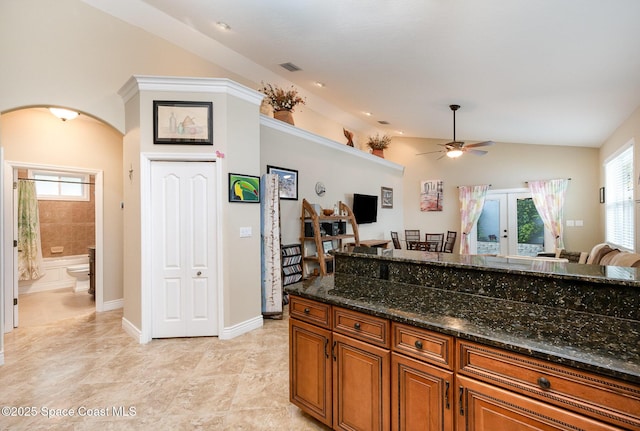 210 Sutton St, Rockledge, FL 32955 - kitchen with brown cabinetry, arched walkways, ceiling fan, dark stone countertops, and vaulted ceiling
