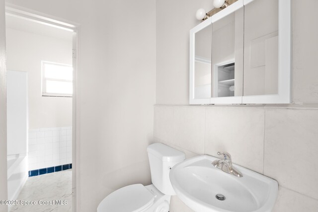 418 N Fiske Blvd, Cocoa, FL 32922 - bathroom featuring a sink, toilet, tile walls, wainscoting, and a tub