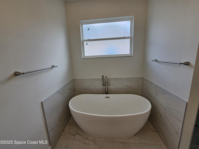 2999 Gaffney Ave SE, Palm Bay, FL 32909 - bathroom with marble look tile flooring, tile walls, a freestanding tub, and wainscoting