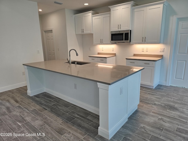 431 Falls Church St SW, Palm Bay, FL 32908 - kitchen with stainless steel microwave, wood finish floors, a kitchen island with sink, recessed lighting, and white cabinets