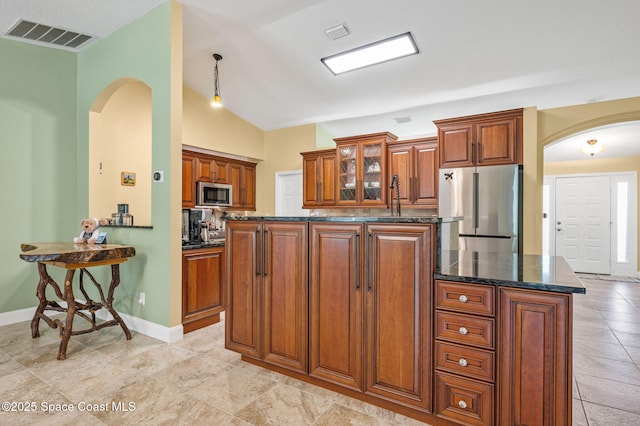 1317 Mohegan Ter SE, Palm Bay, FL 32909 - kitchen with stainless steel appliances, arched walkways, brown cabinetry, glass insert cabinets, and dark stone counters
