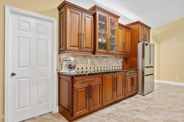 1317 Mohegan Ter SE, Palm Bay, FL 32909 - kitchen featuring freestanding refrigerator, brown cabinets, backsplash, dark stone counters, and glass insert cabinets