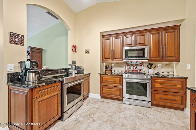 1317 Mohegan Ter SE, Palm Bay, FL 32909 - kitchen with stainless steel appliances, lofted ceiling, arched walkways, dark stone countertops, and brown cabinets