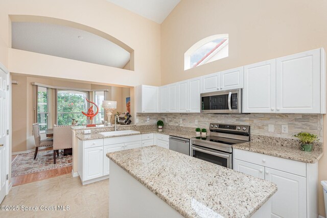 570 Shell Cove Dr, Melbourne, FL 32940 - kitchen featuring stainless steel appliances, a sink, high vaulted ceiling, decorative backsplash, and white cabinetry