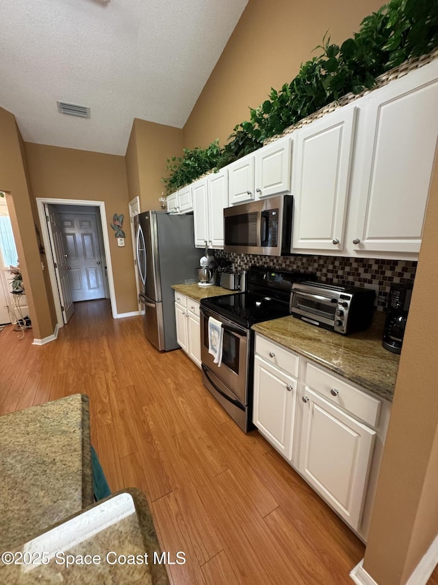 157 Lehigh Ave SE, Palm Bay, FL 32909 - kitchen featuring appliances with stainless steel finishes, light wood-style floors, decorative backsplash, white cabinets, and vaulted ceiling