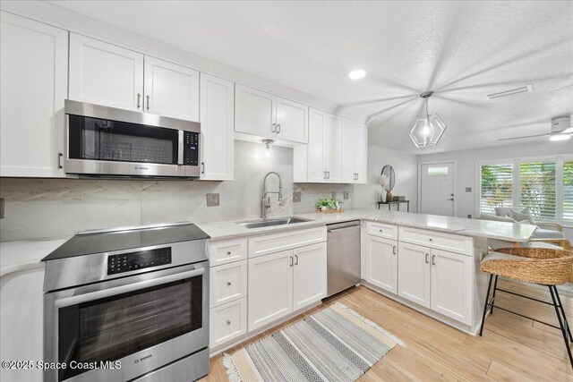 629 Verbenia Dr, Satellite Beach, FL 32937 - kitchen featuring stainless steel appliances, a sink, white cabinets, a peninsula, and light wood-style flooring