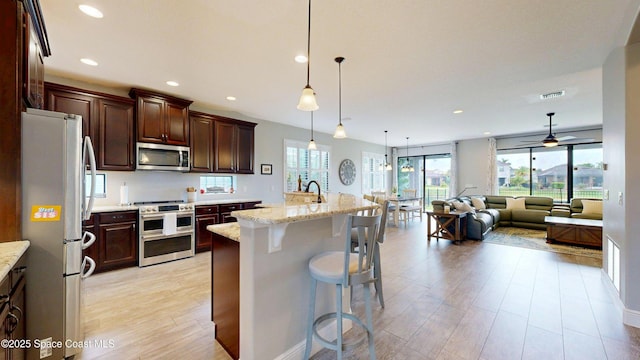 8051 Strom Park Dr, Melbourne, FL 32940 - kitchen featuring stainless steel appliances, open floor plan, light wood finished floors, a kitchen bar, and hanging light fixtures