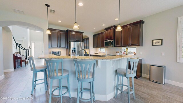 8051 Strom Park Dr, Melbourne, FL 32940 - kitchen with stainless steel appliances, arched walkways, light wood-type flooring, dark brown cabinets, and light stone countertops