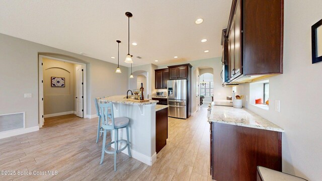 8051 Strom Park Dr, Melbourne, FL 32940 - kitchen featuring stainless steel refrigerator with ice dispenser, arched walkways, a center island with sink, a kitchen bar, and light wood-style flooring