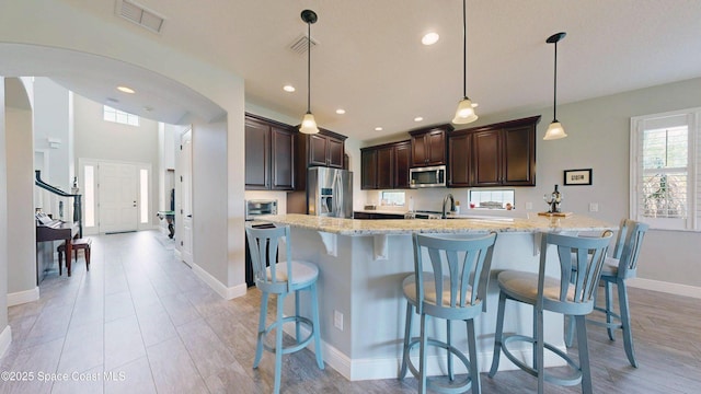 8051 Strom Park Dr, Melbourne, FL 32940 - kitchen featuring appliances with stainless steel finishes, dark brown cabinets, light stone counters, a breakfast bar area, and recessed lighting